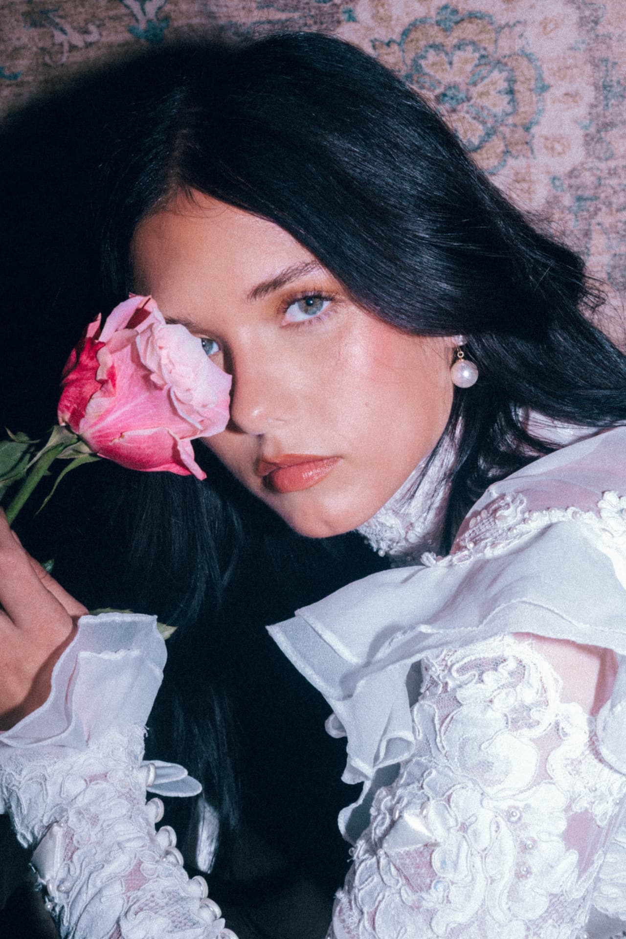 A bride holding a pink rose beside her face