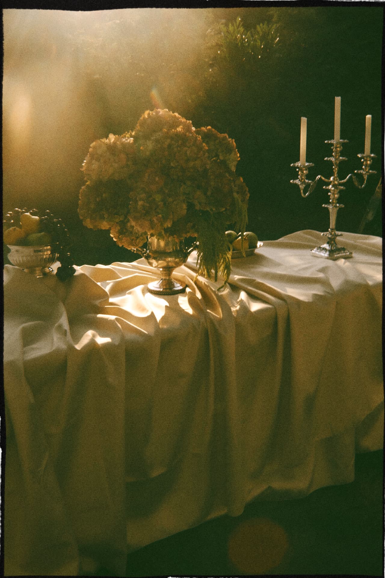 A candlelit table draped in ivory linen with hydrangeas in a silver urn